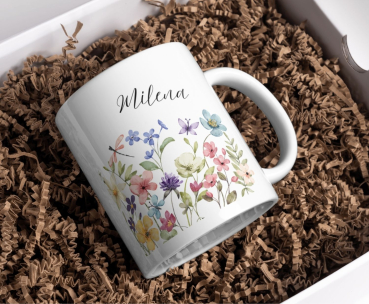 Weiße Keramiktasse mit floralen Aquarellblumen und personalisiertem Namen „Milena“, stilvoll arrangiert in einer Geschenkbox mit brauner Holzwolle.